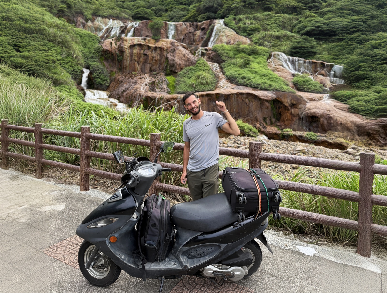 Filippo with his loaded scooter beside a waterfall in Taiwan